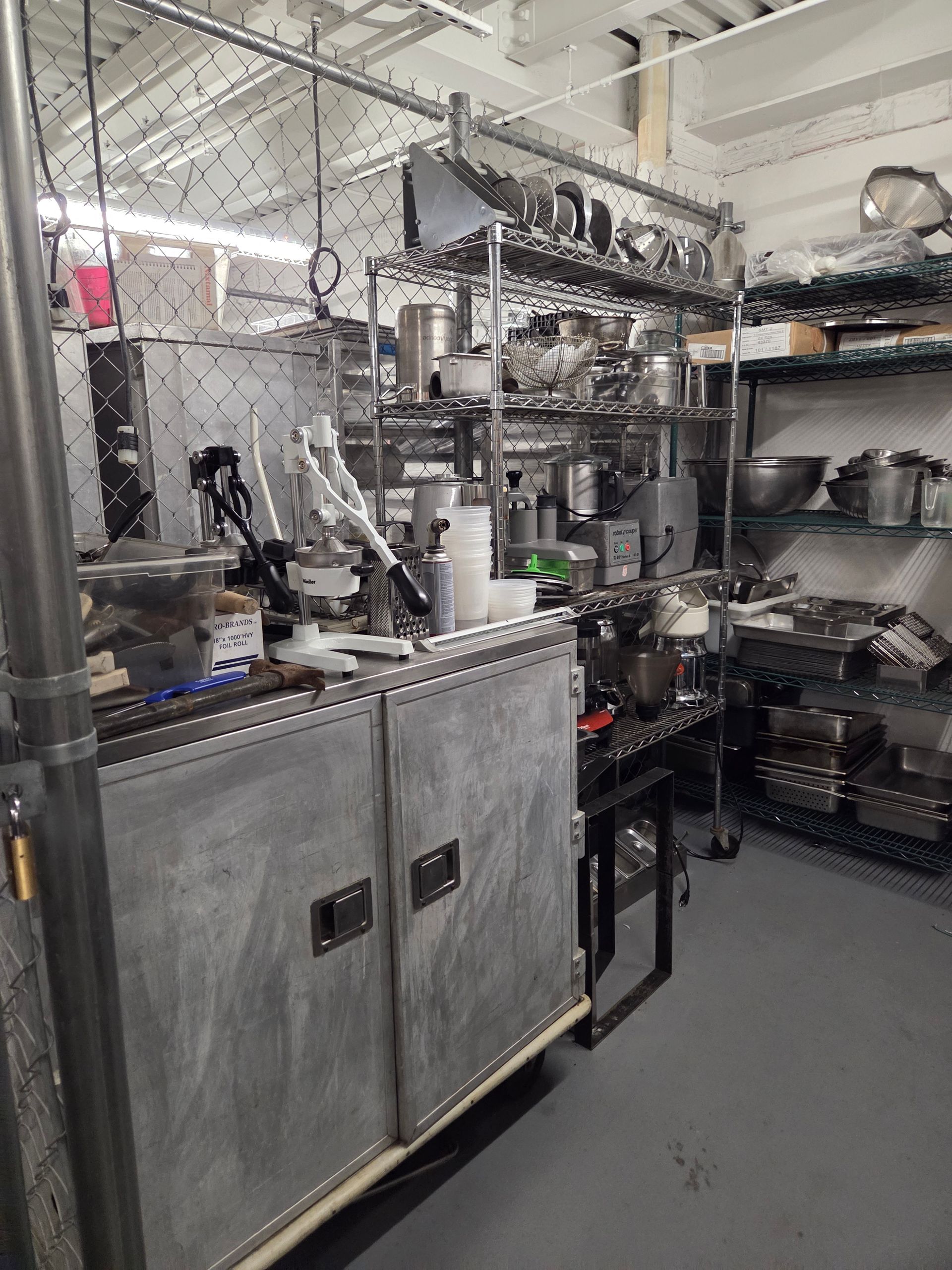 A cluttered commercial kitchen with stainless steel appliances, shelves, and various utensils.