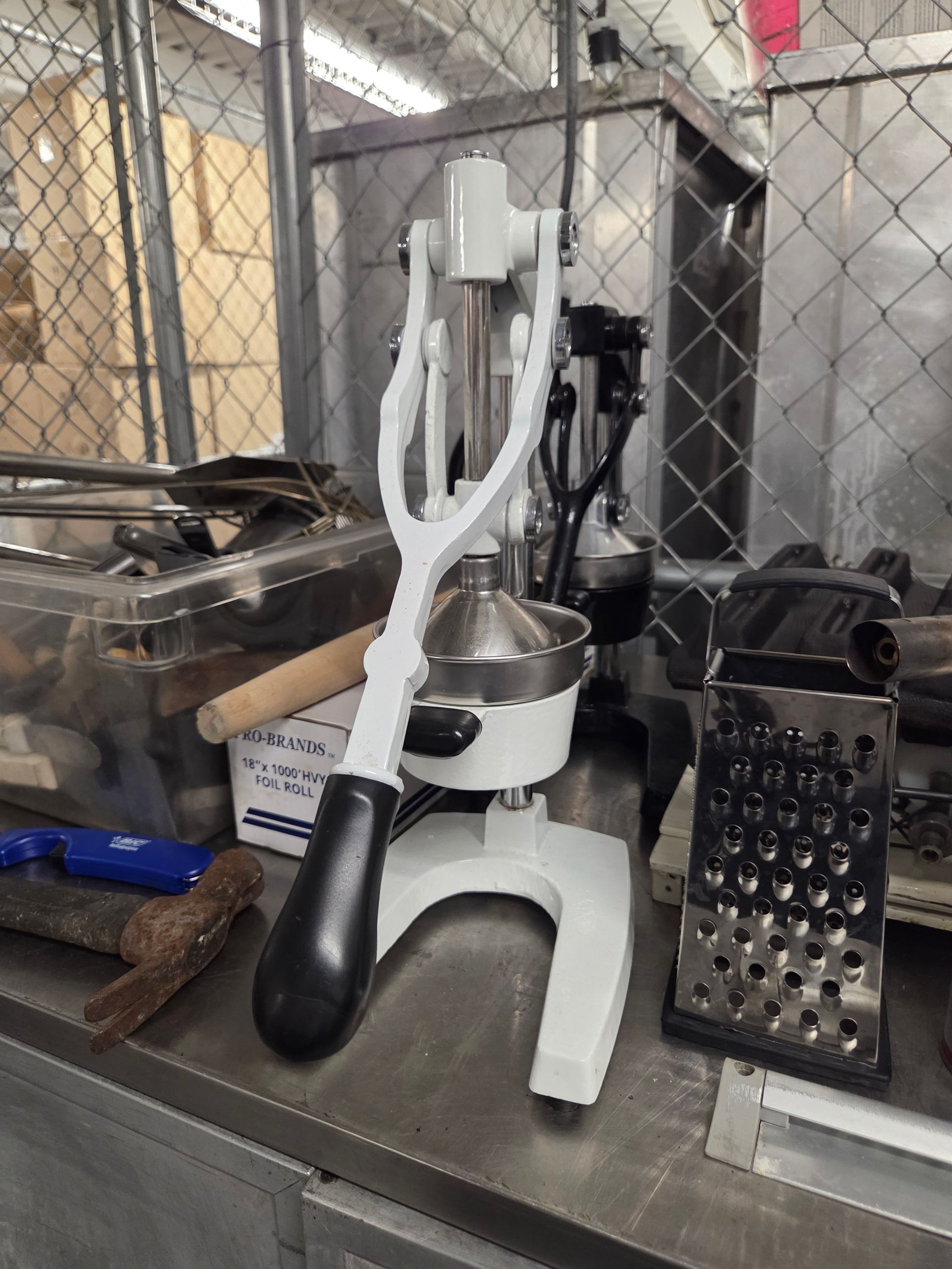White citrus juicer on a metal surface, with a grater and tools nearby.