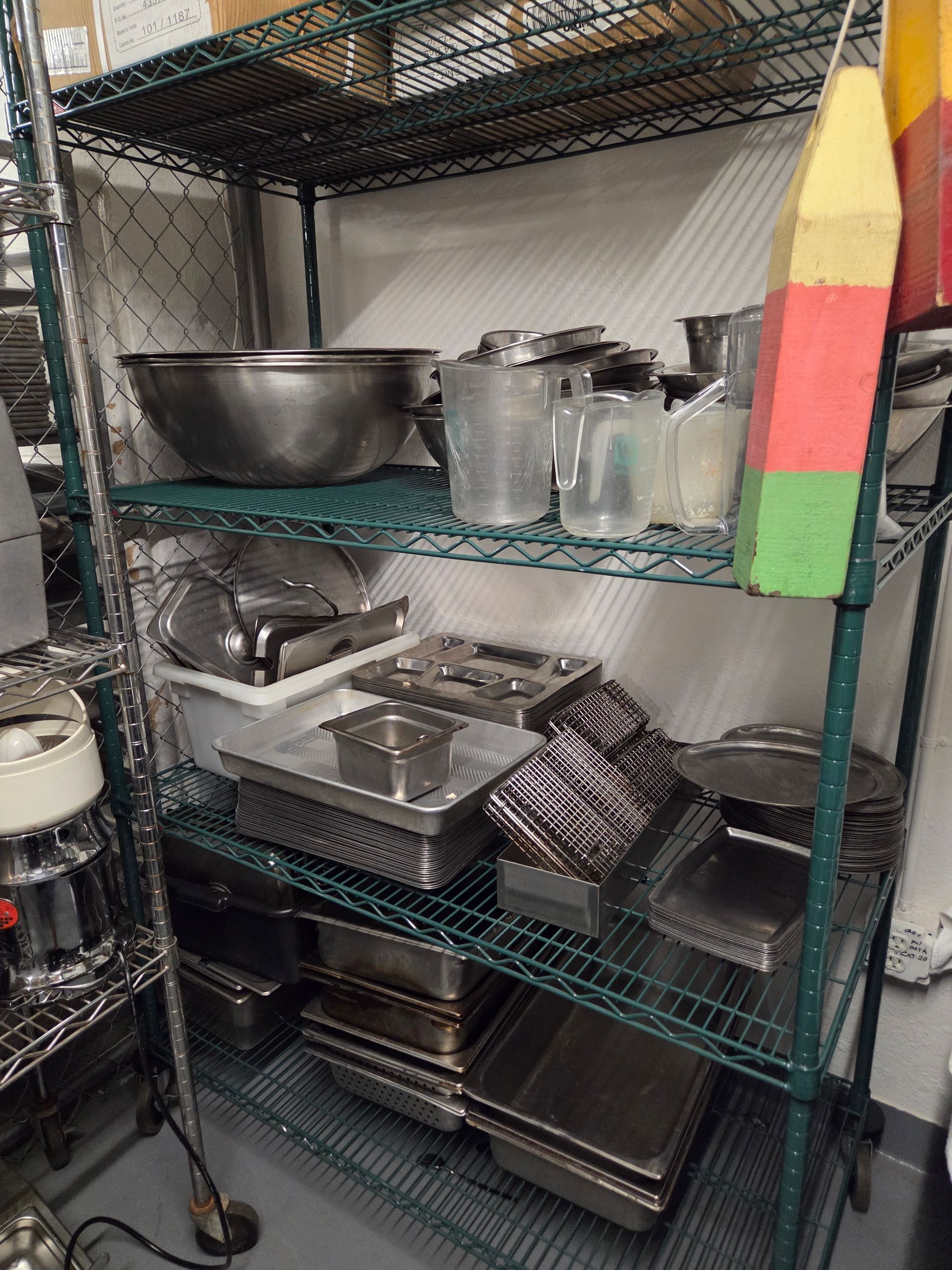 Metal shelving unit in a kitchen filled with various stainless steel containers and utensils.