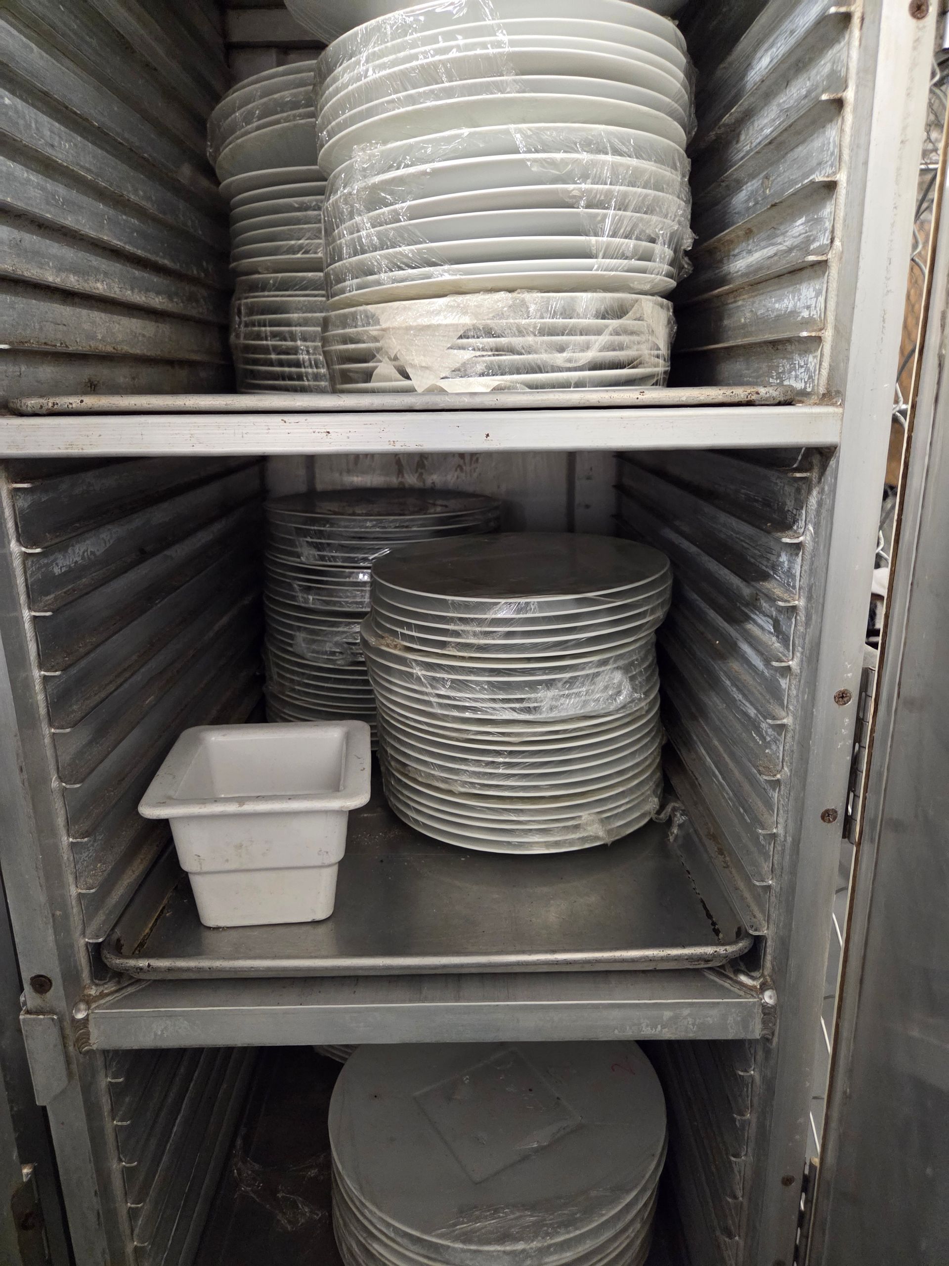 Stacked metal plates and a container inside a metal warming cabinet.