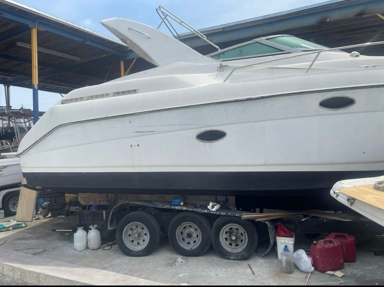 White motorboat on a trailer at a shipyard, under a covered area.