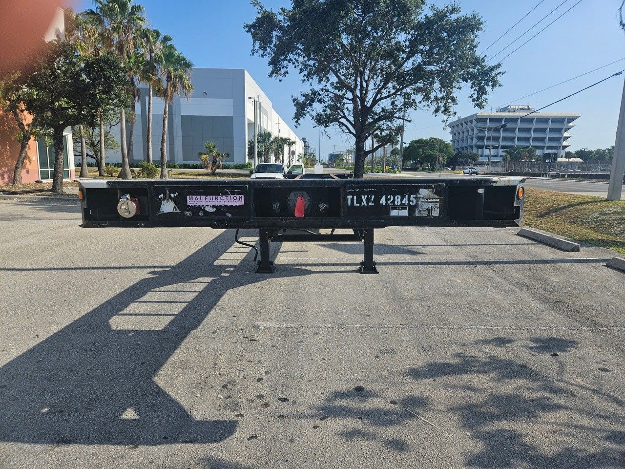 Black empty container chassis parked on asphalt lot with buildings in the background.