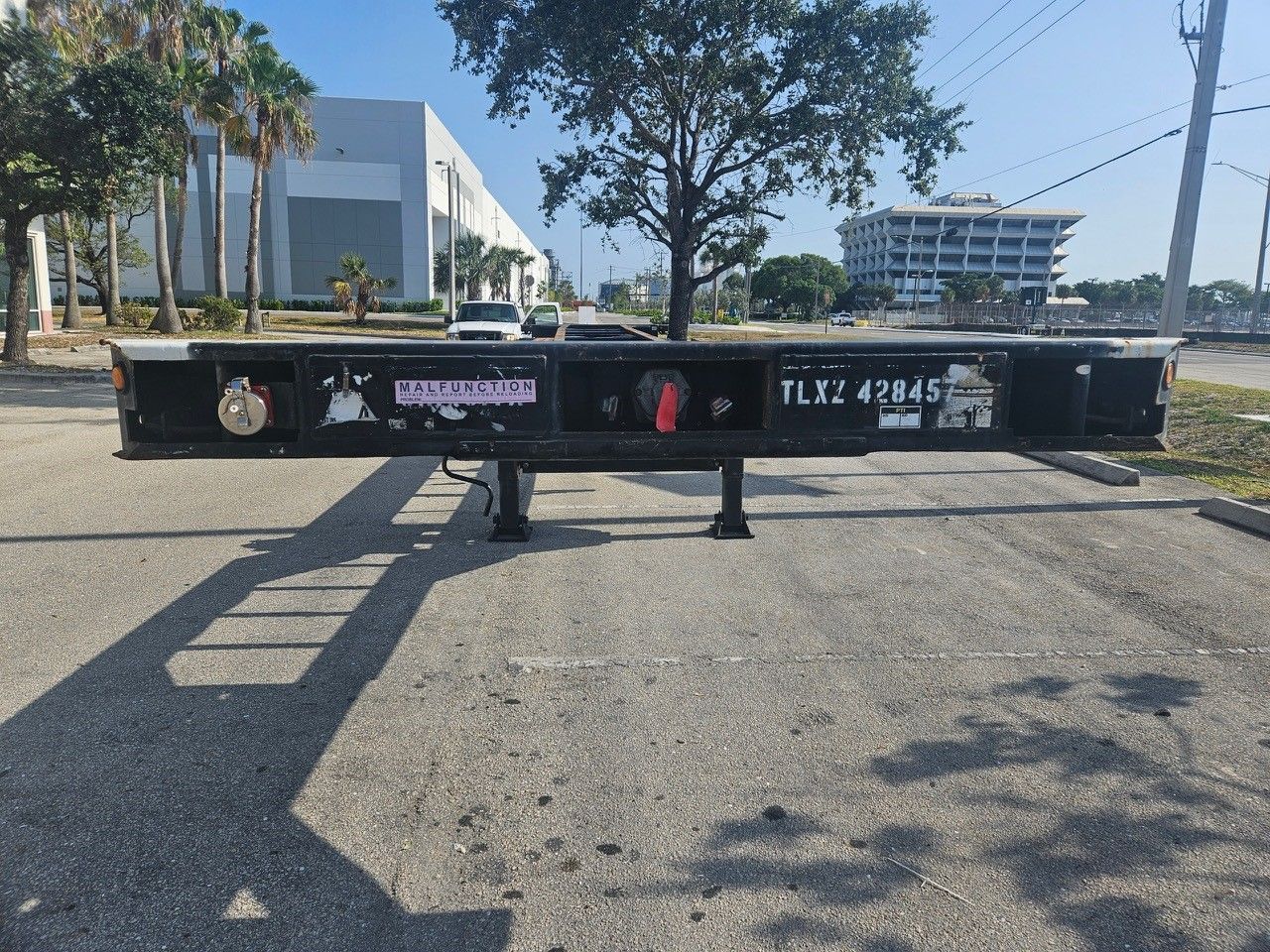 Black trailer chassis on pavement with a building backdrop.