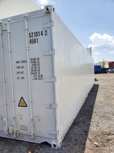 White refrigerated shipping container on a gravel lot, under a sunny sky.