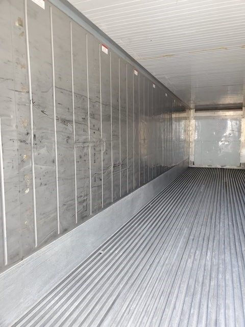 Interior of a refrigerated trailer with ribbed flooring, vertical wall panels, and a white ceiling.