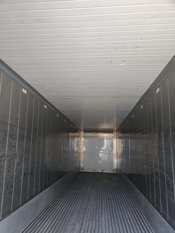 Empty refrigerated semi-trailer interior. Metal walls, ribbed floor, white ceiling, viewed from the back.
