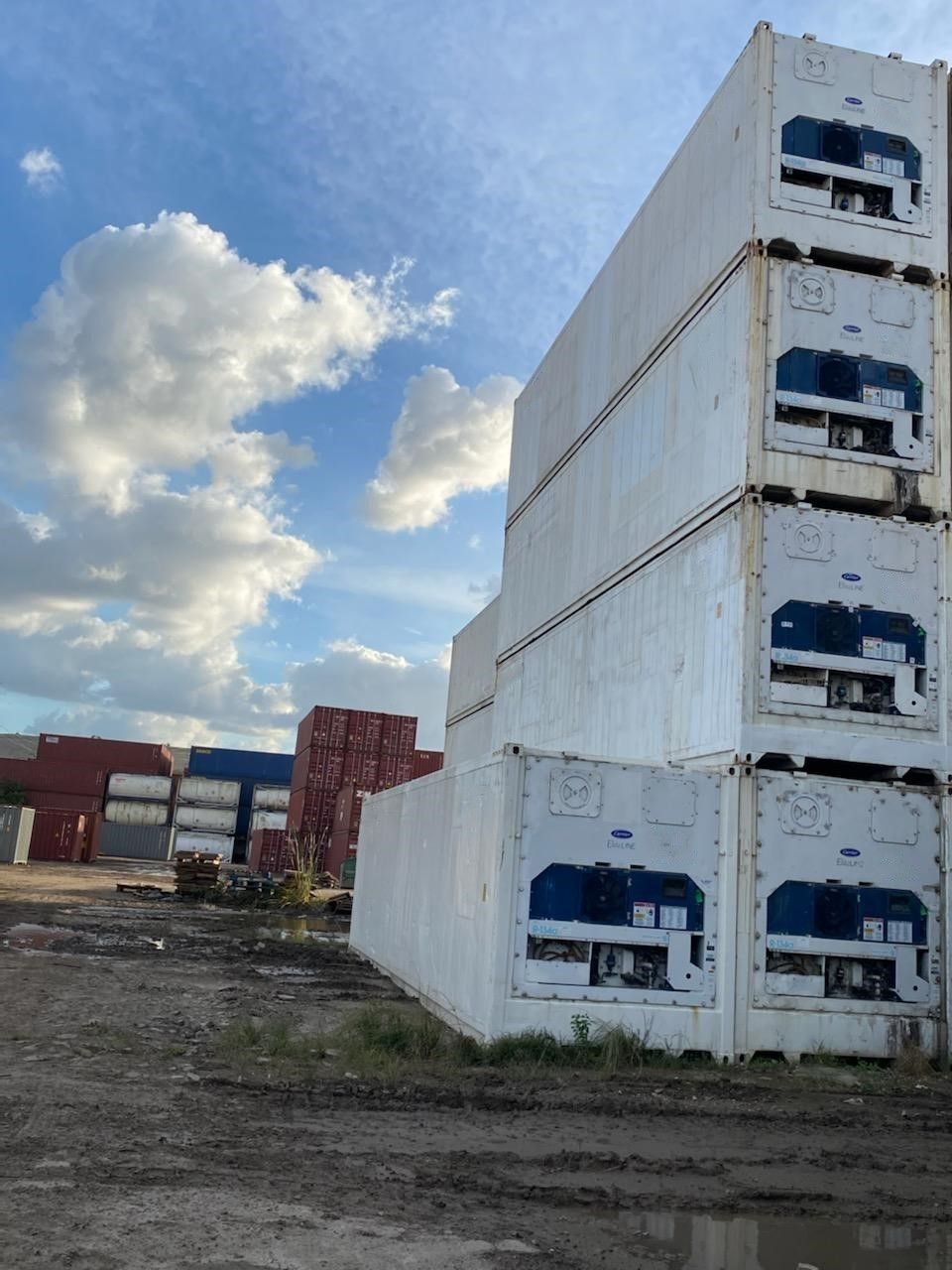 Stacked white refrigerated shipping containers in a lot under a cloudy sky.