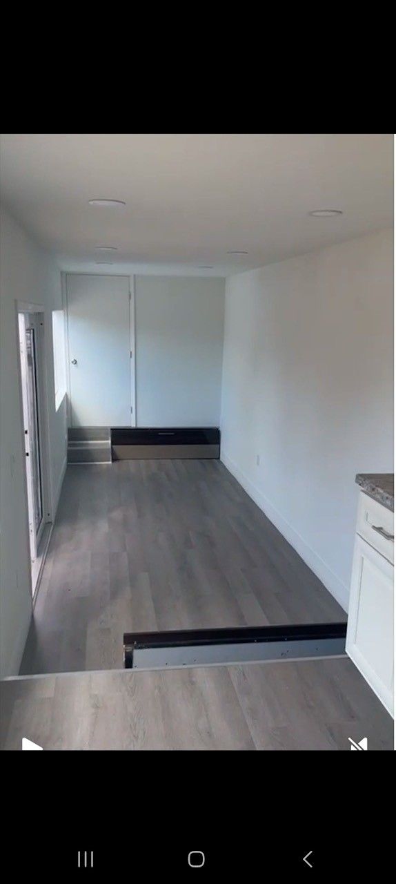 Interior view of a narrow room with light gray wood flooring, white walls, and a doorway.