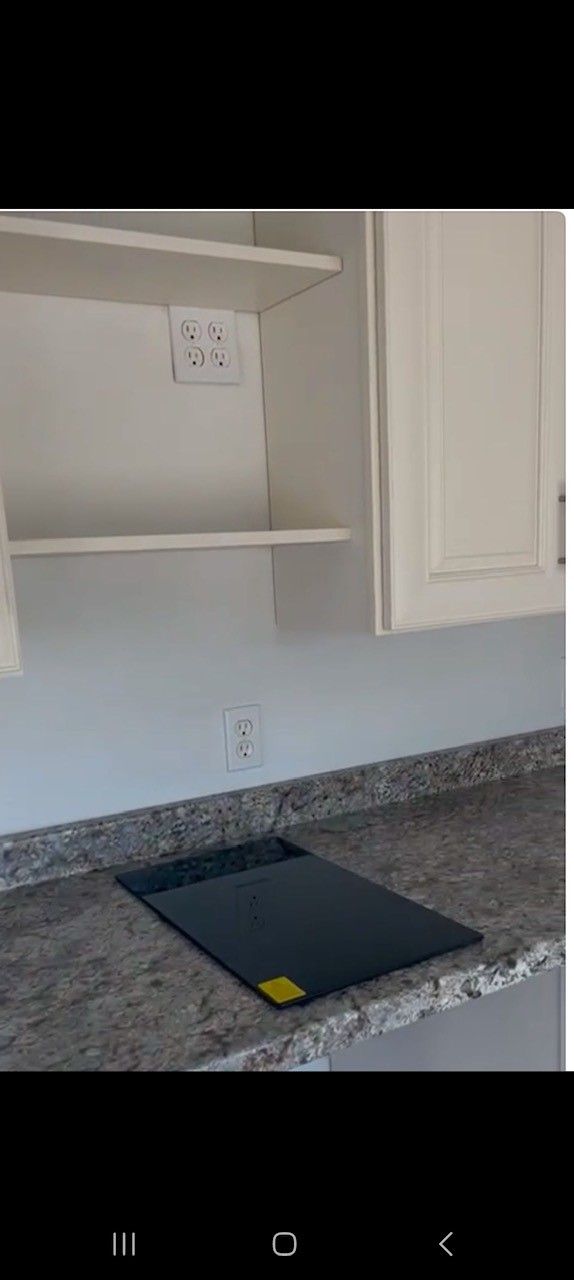 Kitchen countertop with stove top and cabinets. White cabinets, granite countertop, and a dark stove.