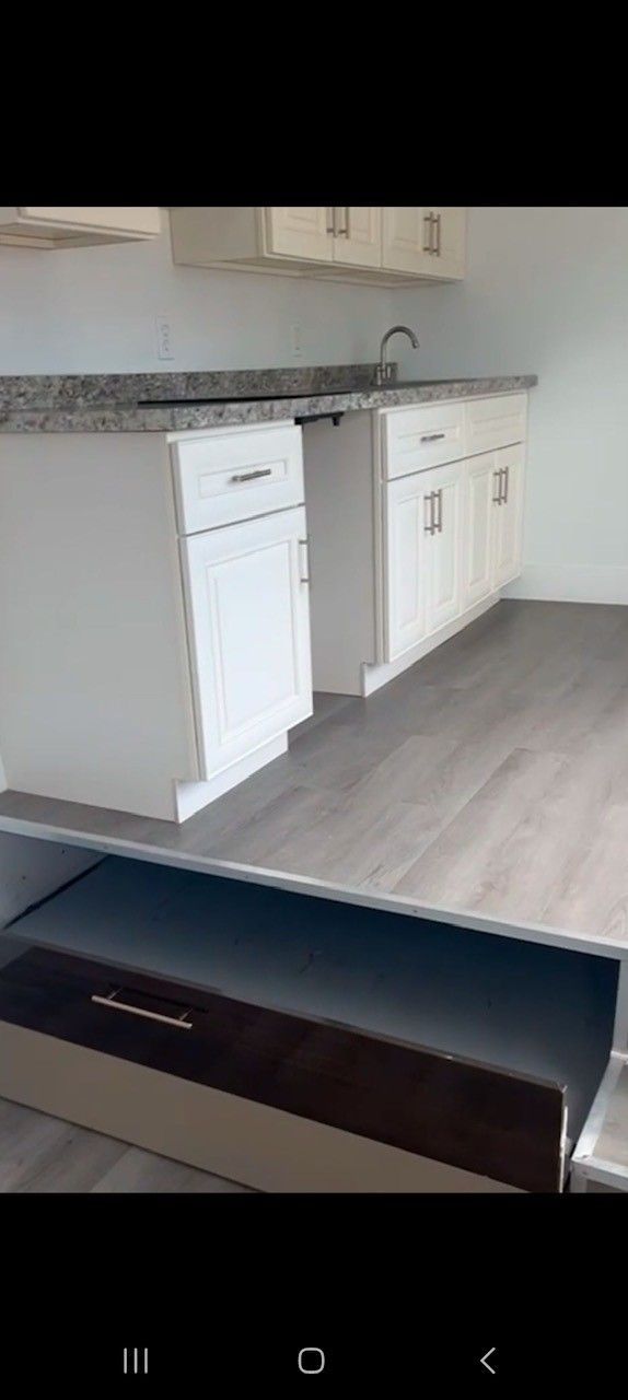 White kitchen cabinets and gray countertop in a room with light gray flooring.
