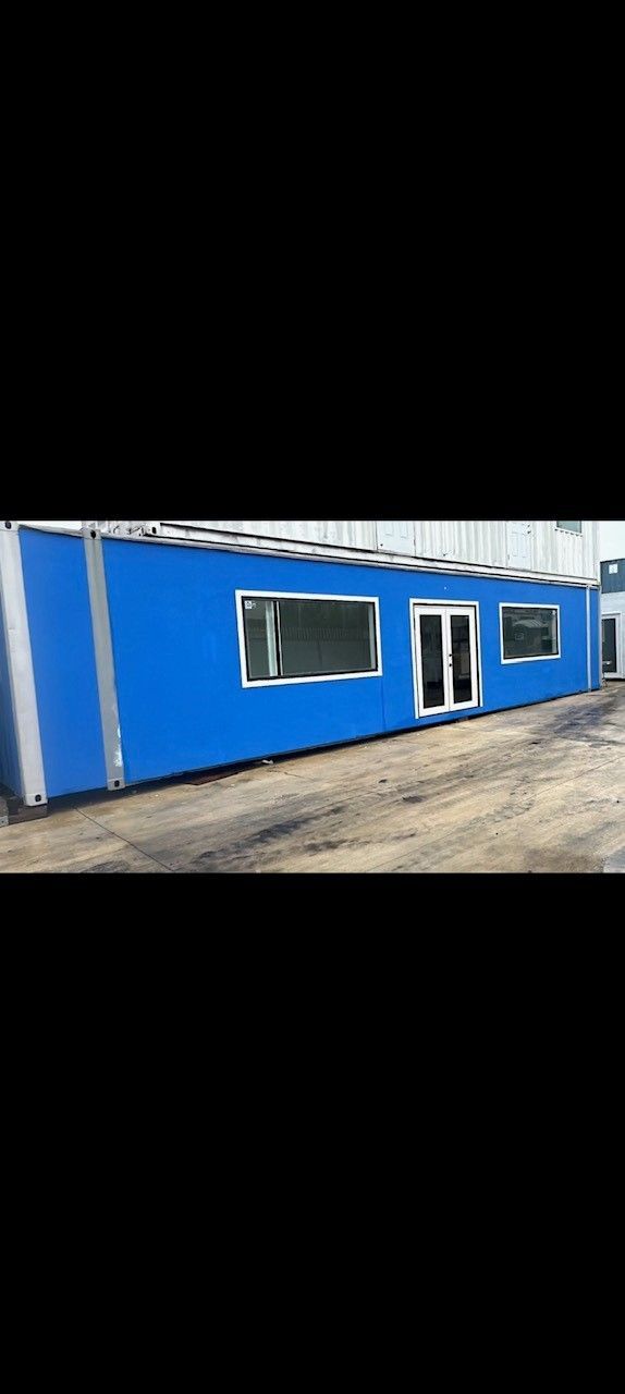 A blue rectangular building with windows and doors, situated outdoors on a dirt ground.