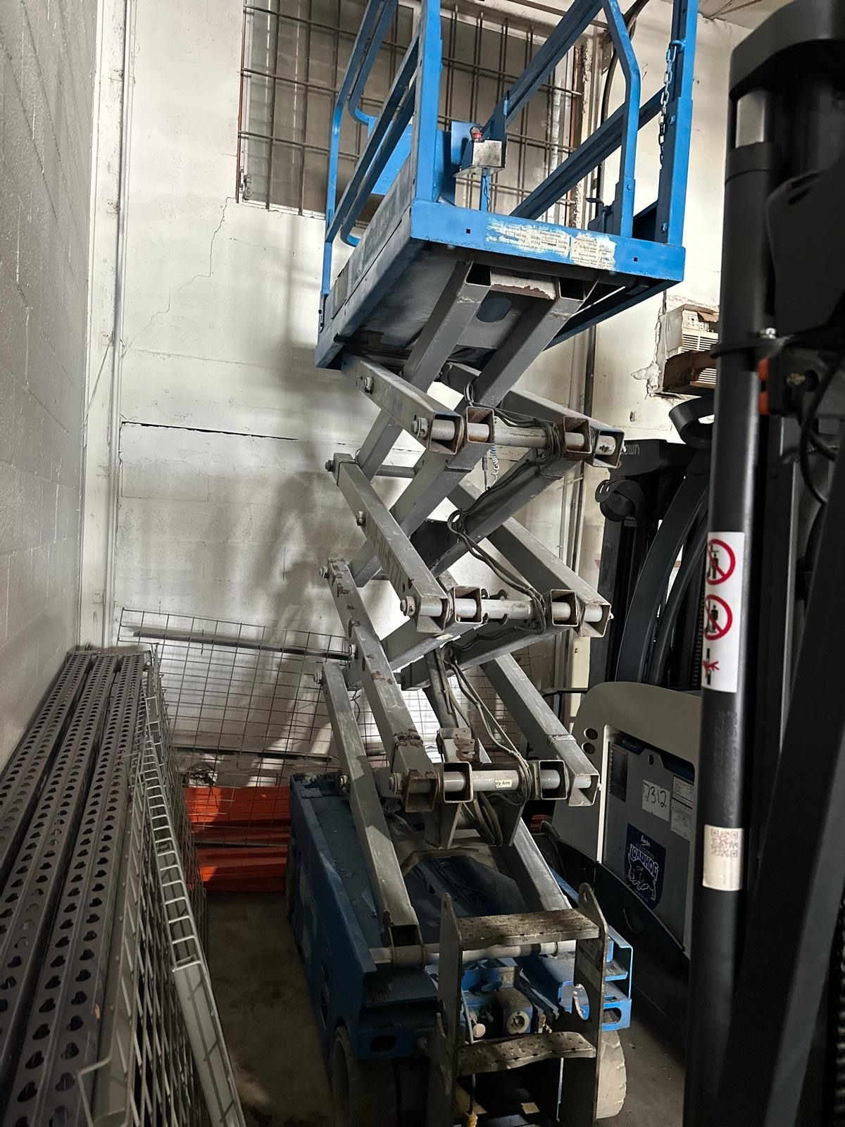 Blue scissor lift in a cluttered indoor setting.