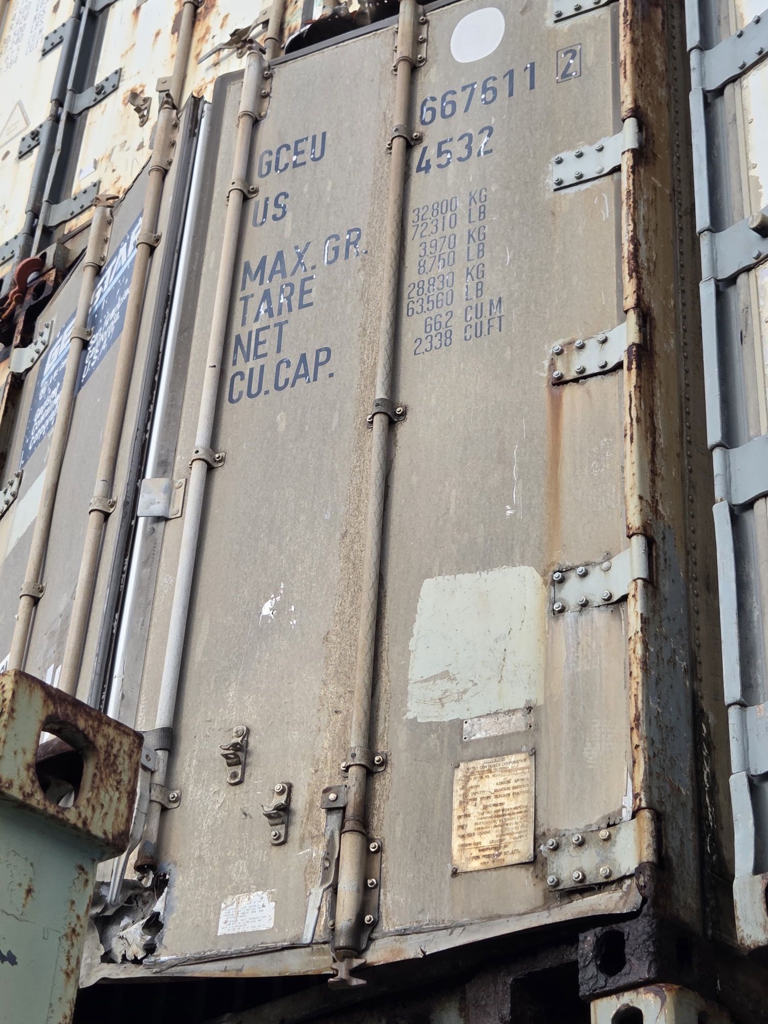 Shipping container, weathered gray with markings, stacked with other containers.