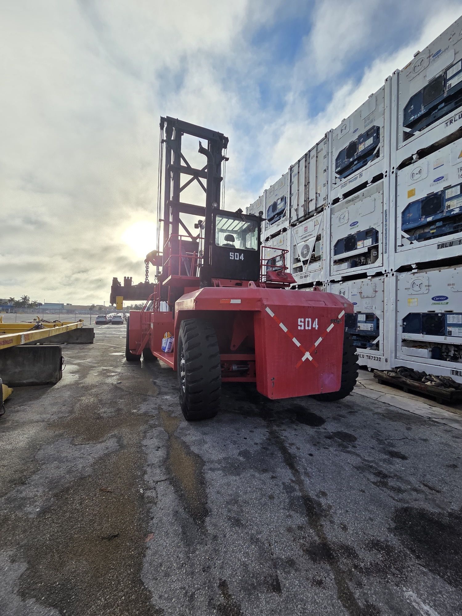 Red container handler truck in front of stacked white containers on a sunny day.