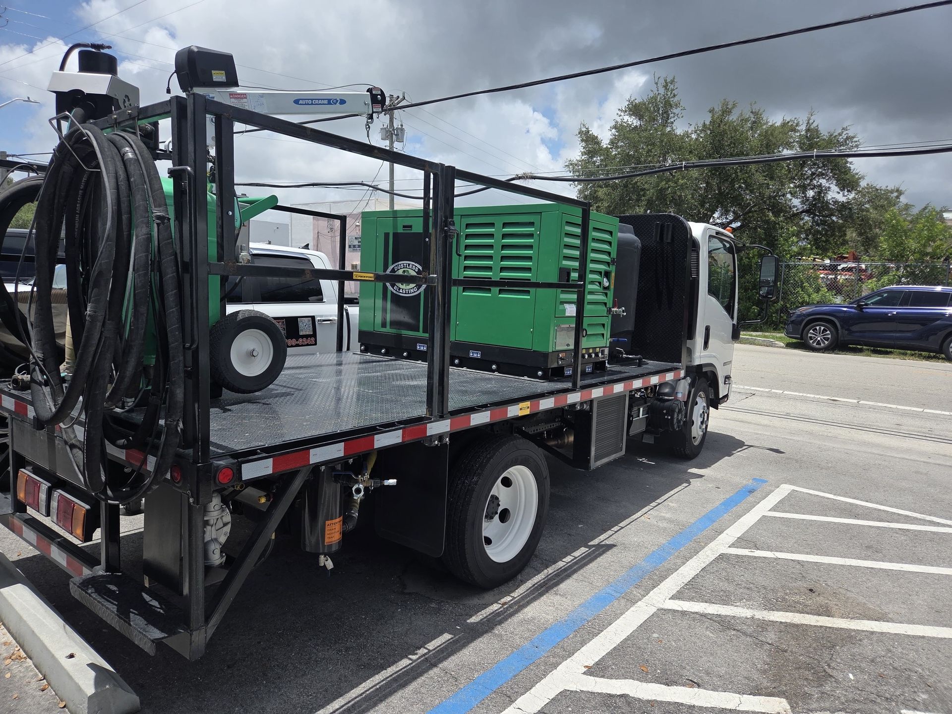 A utility truck with a black frame, green generator, and coiled hoses parked outside.