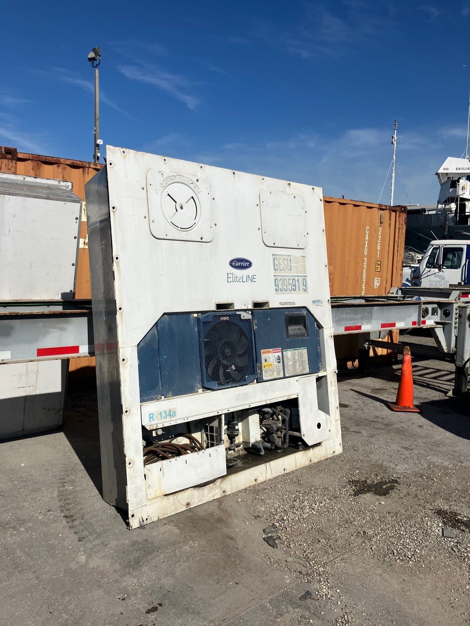 White Carrier refrigeration unit, blue accents, in a shipping yard under a bright blue sky.