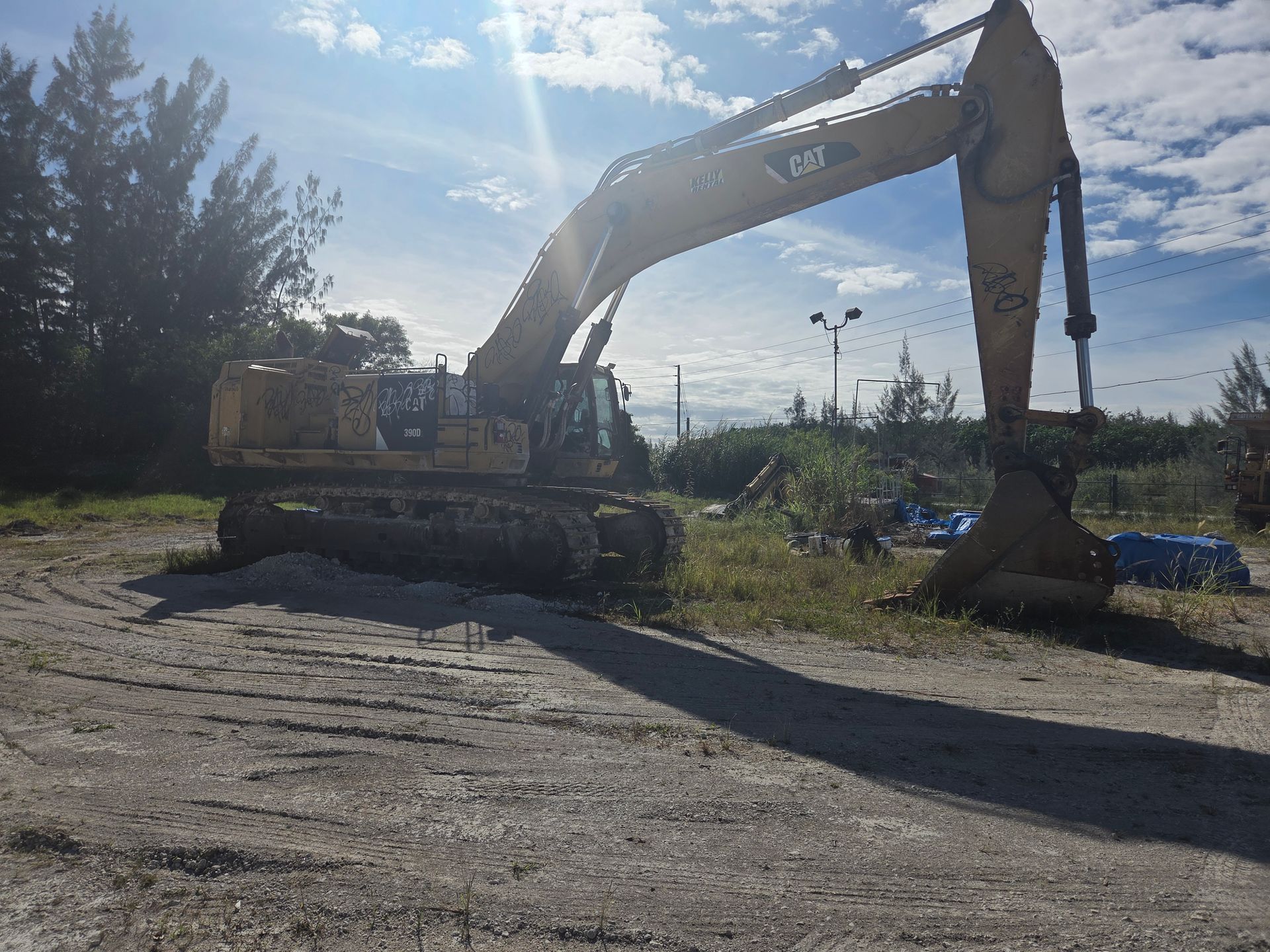 A yellow Caterpillar excavator on a dirt lot under a bright sky.