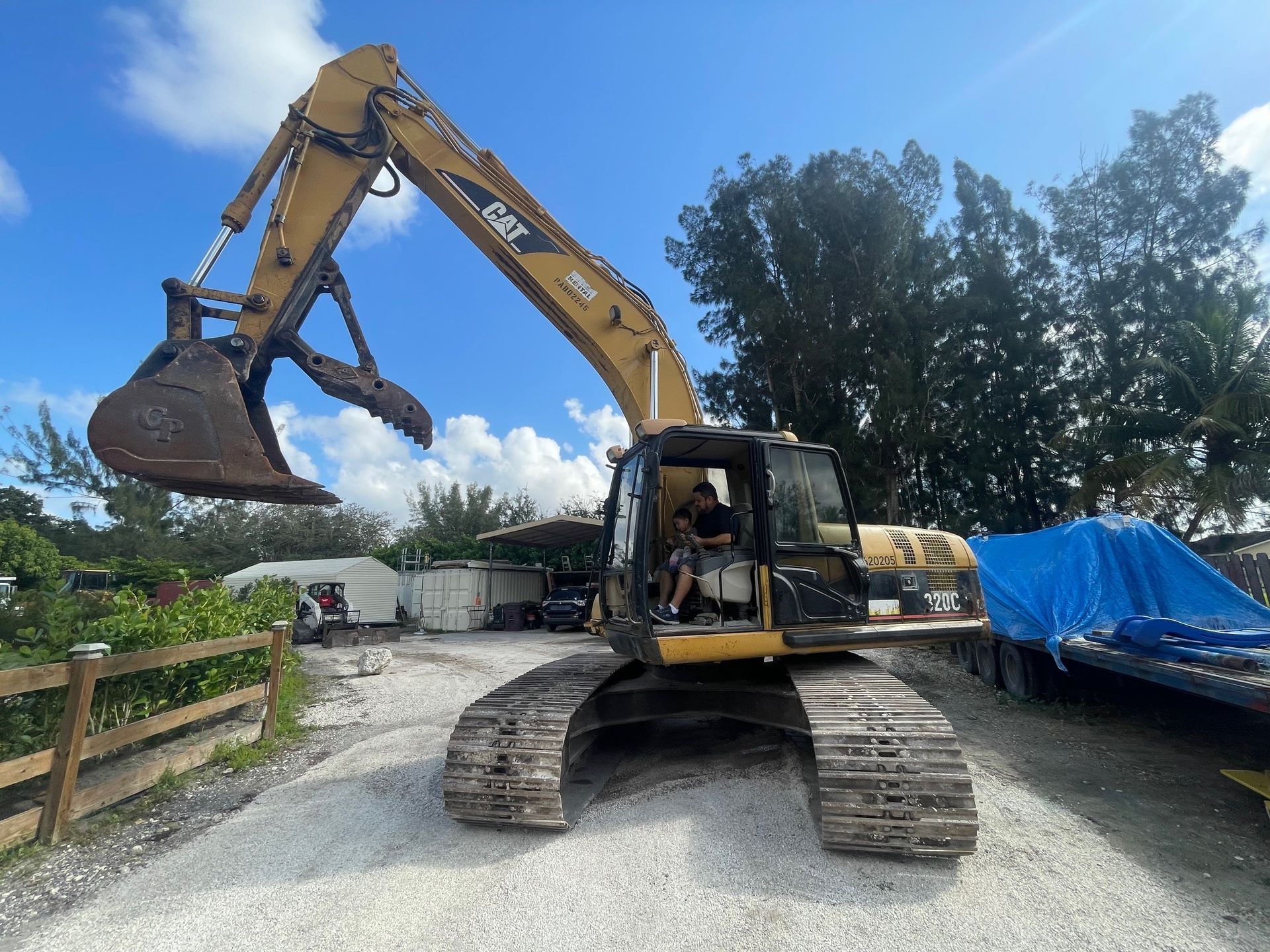 Yellow Caterpillar excavator with claw attachment, raised against blue sky, on gravel.