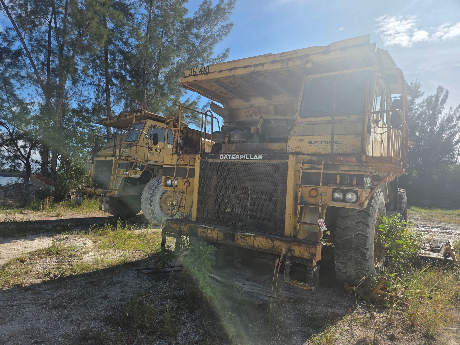 Two weathered yellow Caterpillar mining trucks sit outdoors on a sunny day.
