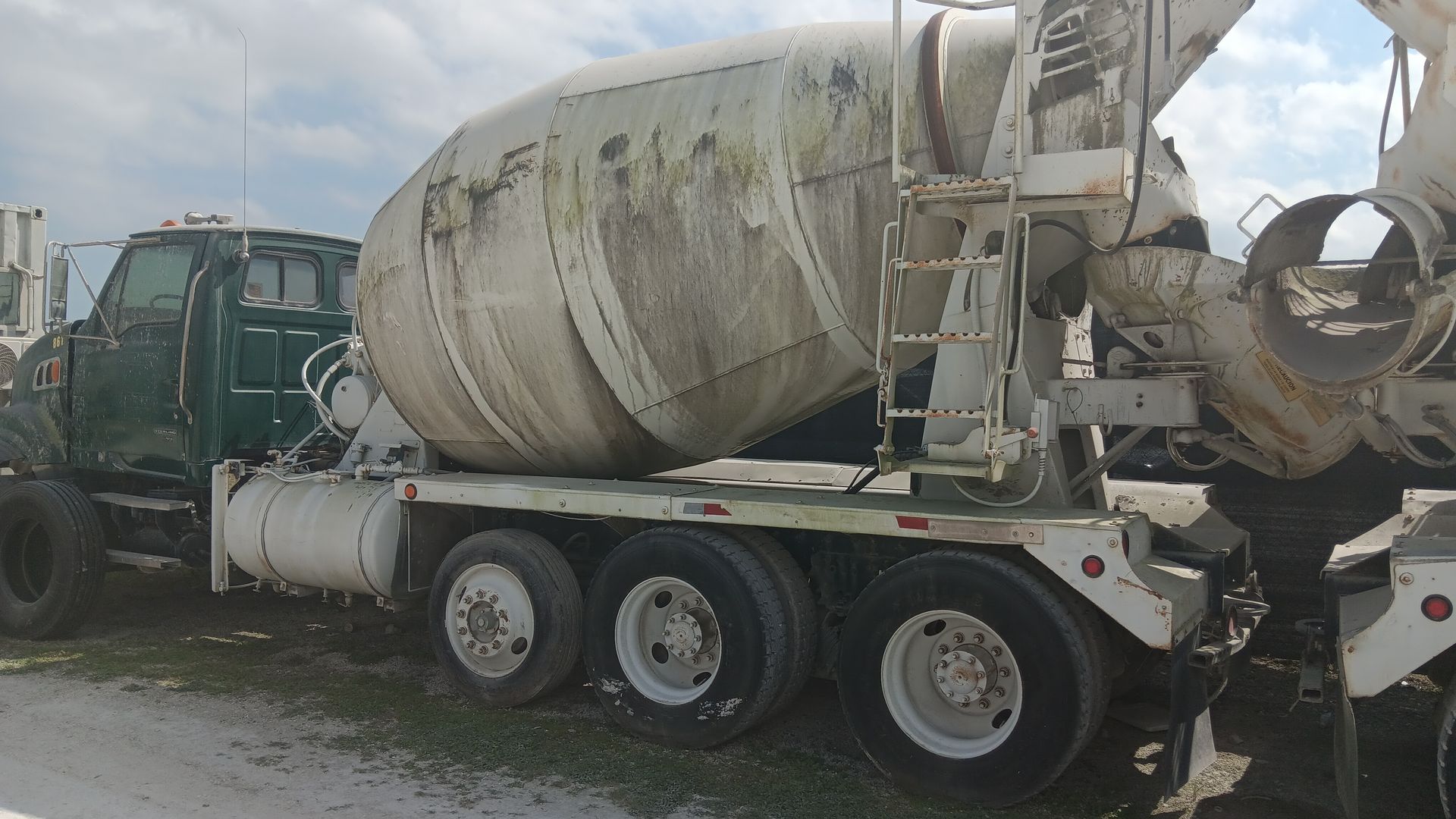 Green and white concrete mixer truck on a grassy field.