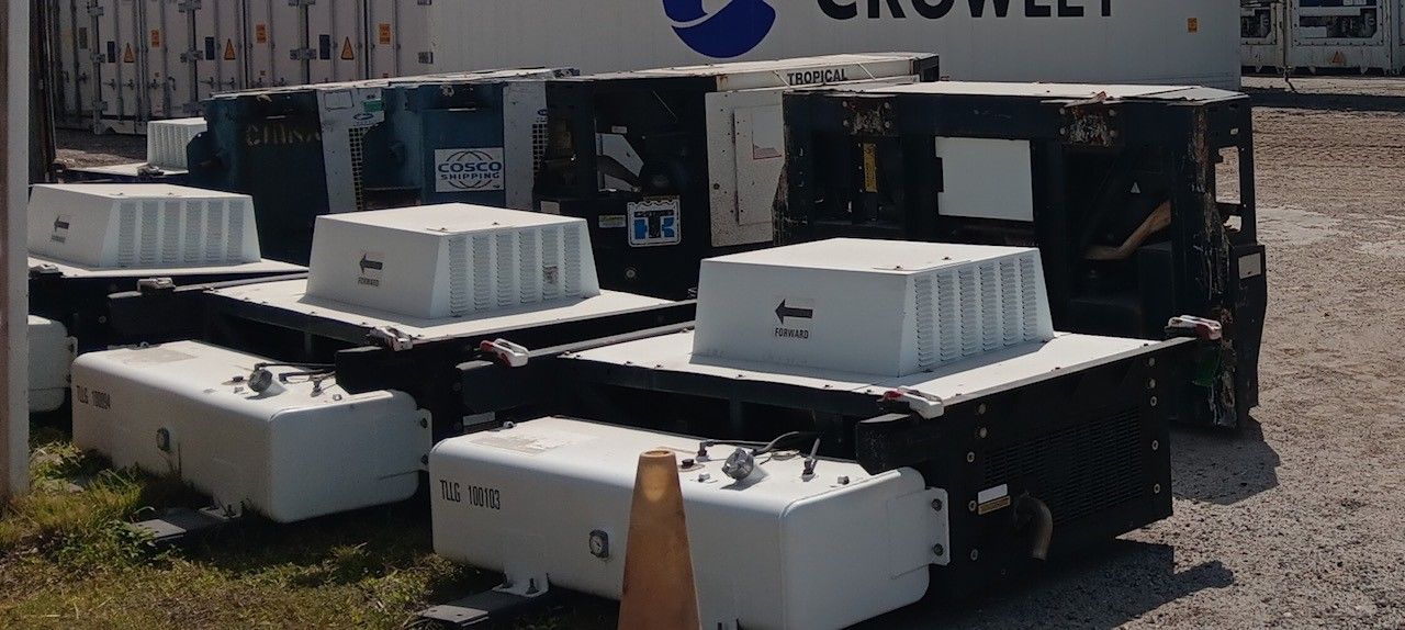 Large, black rectangular containers with white, boxy tops stacked outdoors near a Crowley sign.