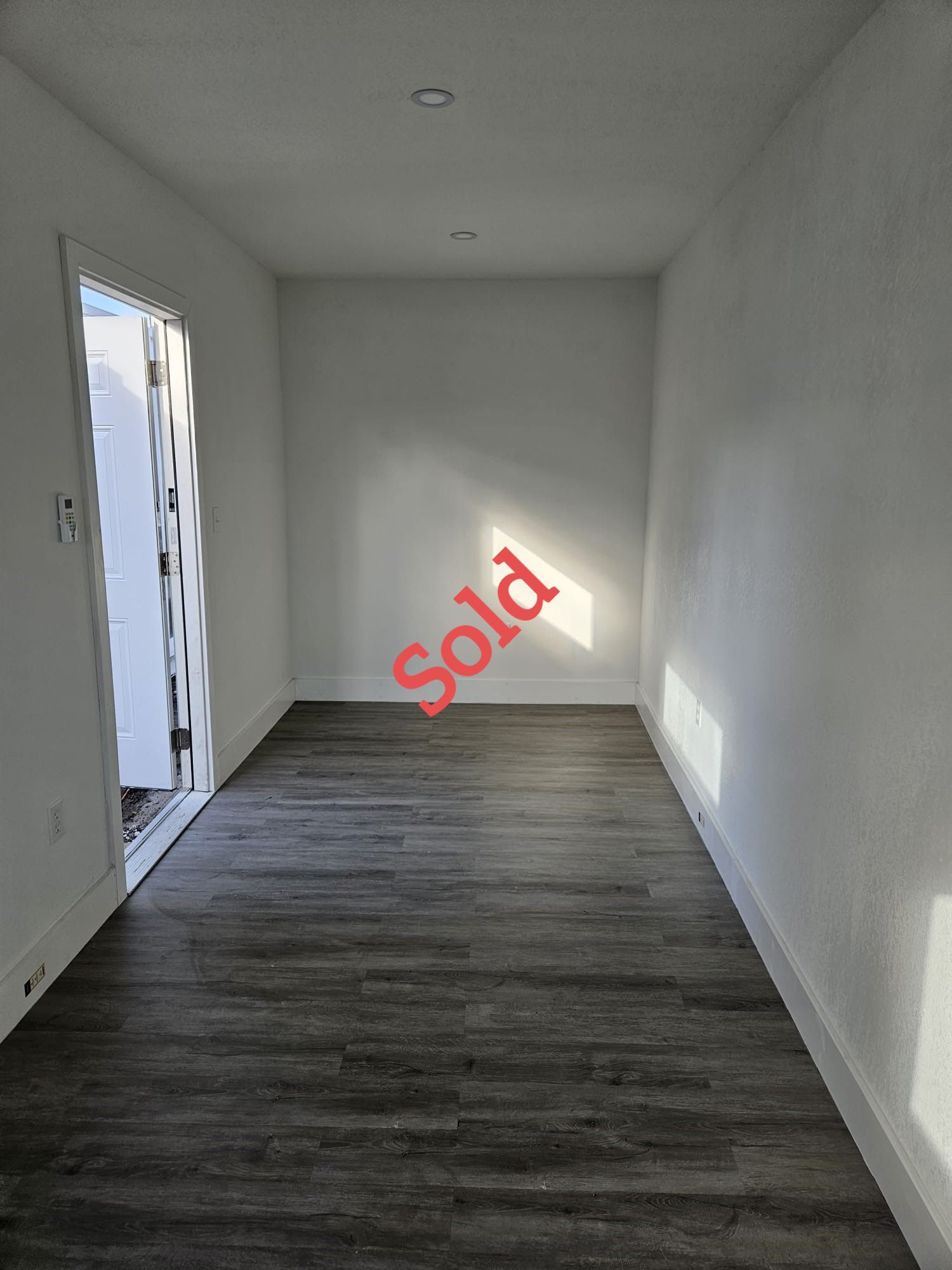 Small empty room with gray flooring, white walls, and a door marked 