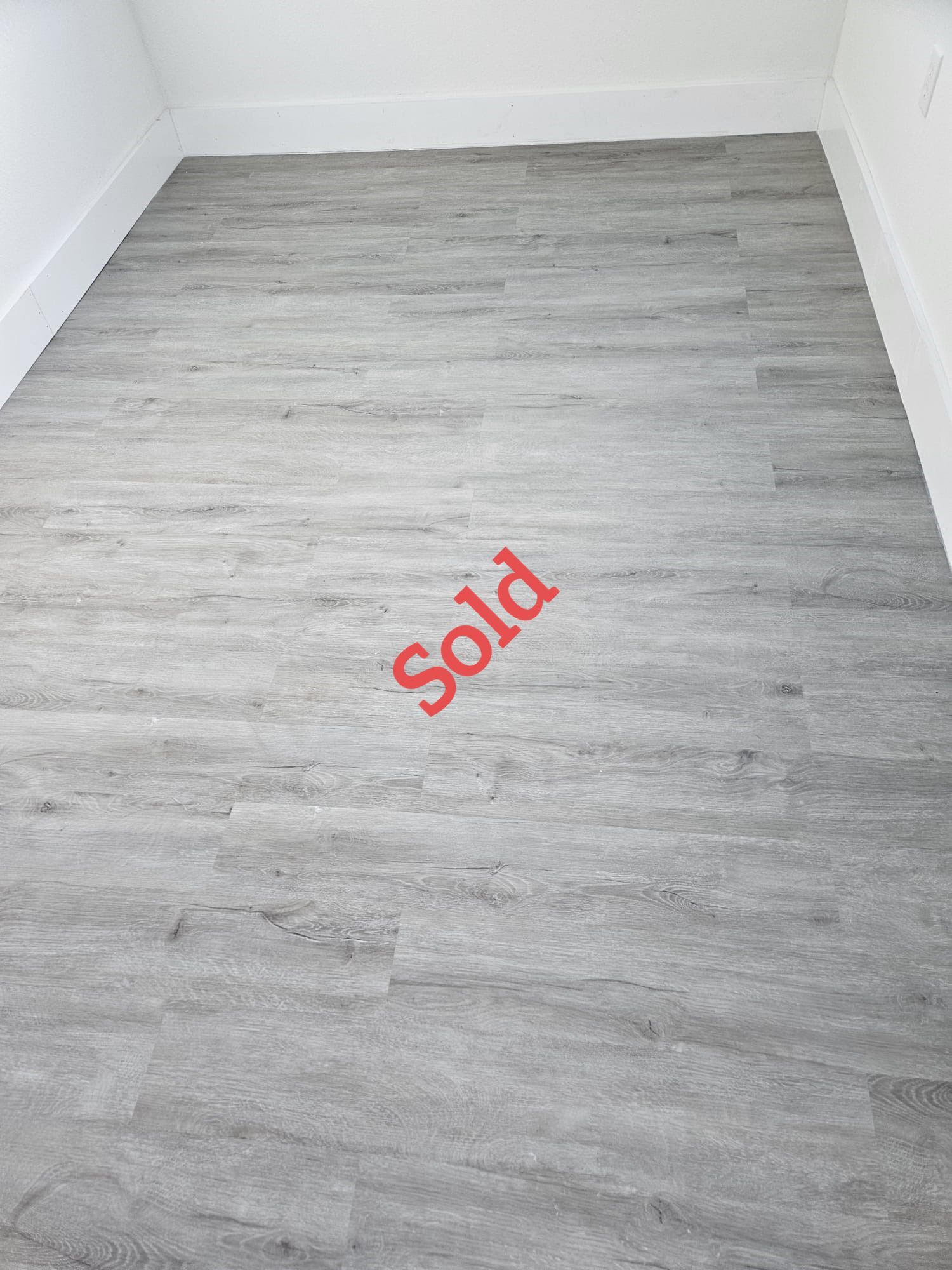 Grey wood-look flooring in a room with white baseboards and walls; 