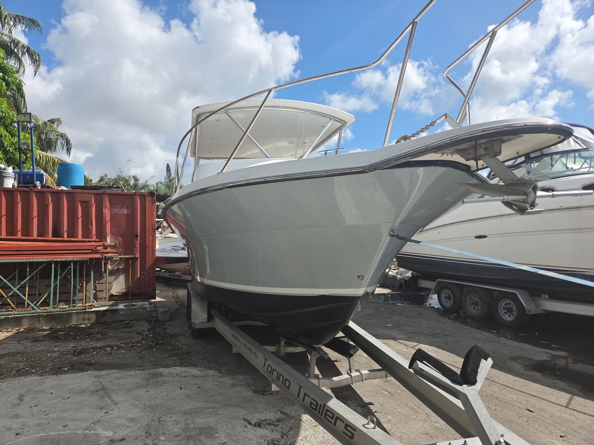 White boat on a trailer, parked outdoors under a cloudy sky.