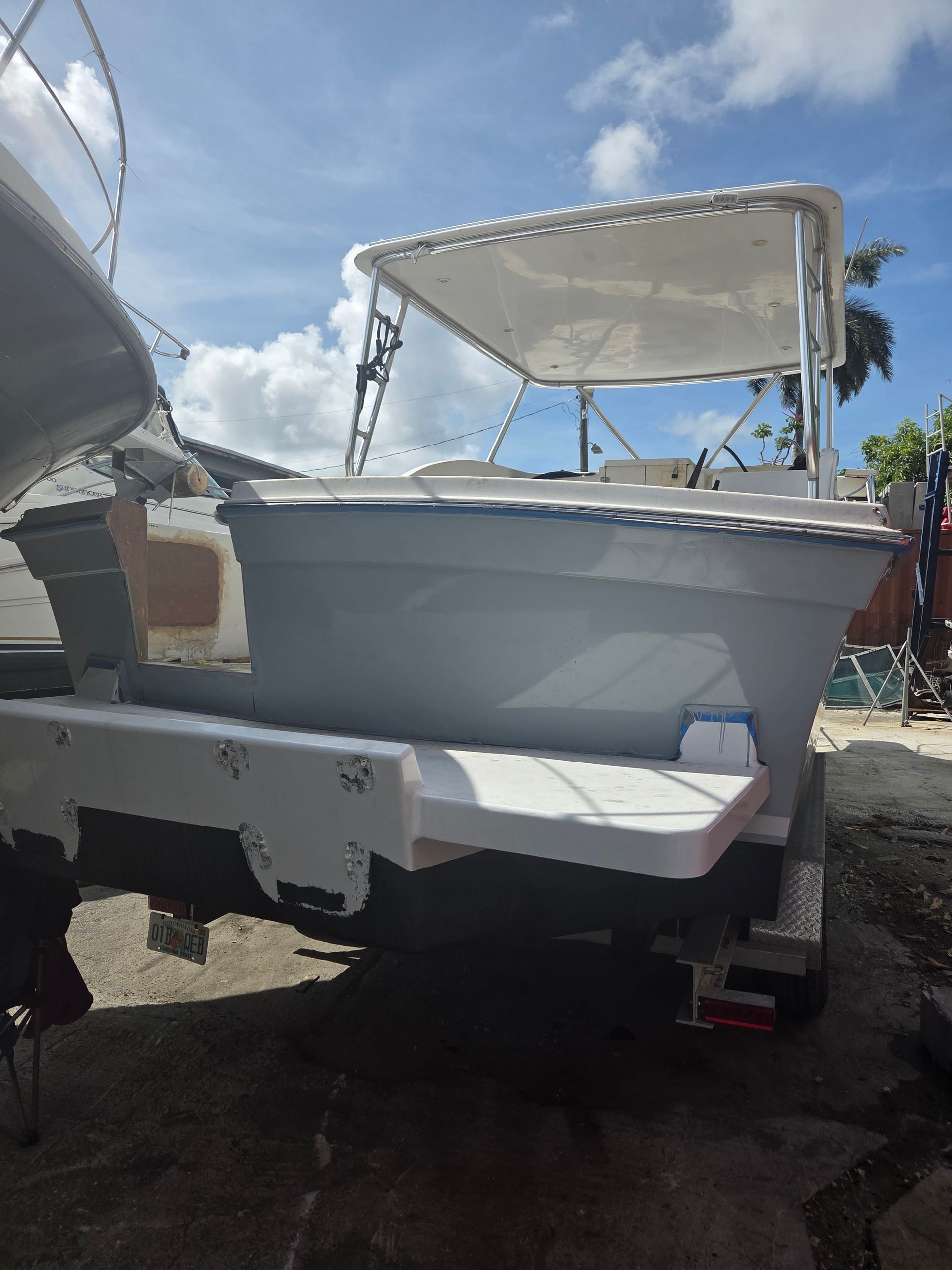 Boat on a trailer, light gray hull, white canopy, blue sky.