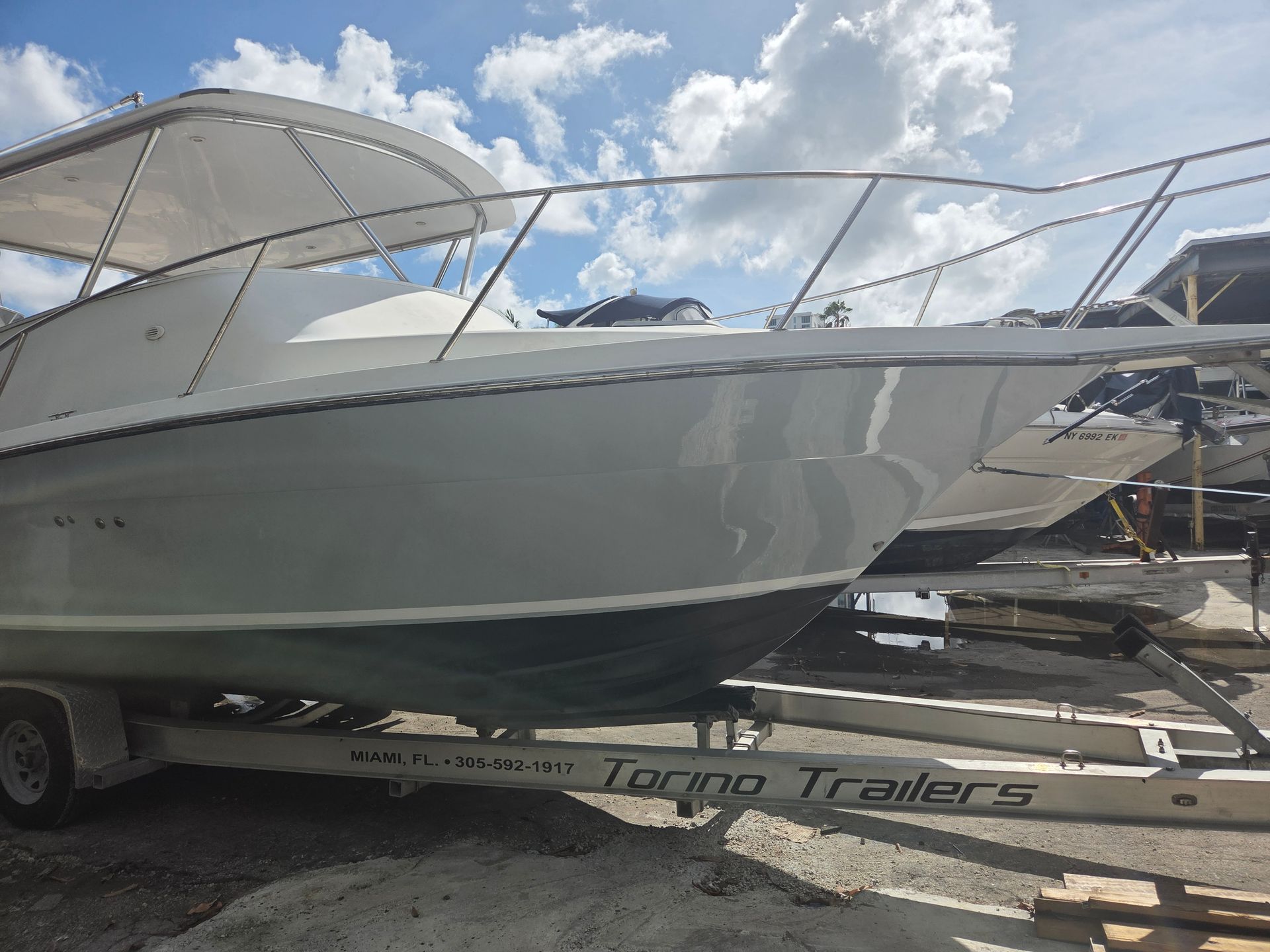 White boat on a trailer under a cloudy sky. Boat has a metal railing and windshield.