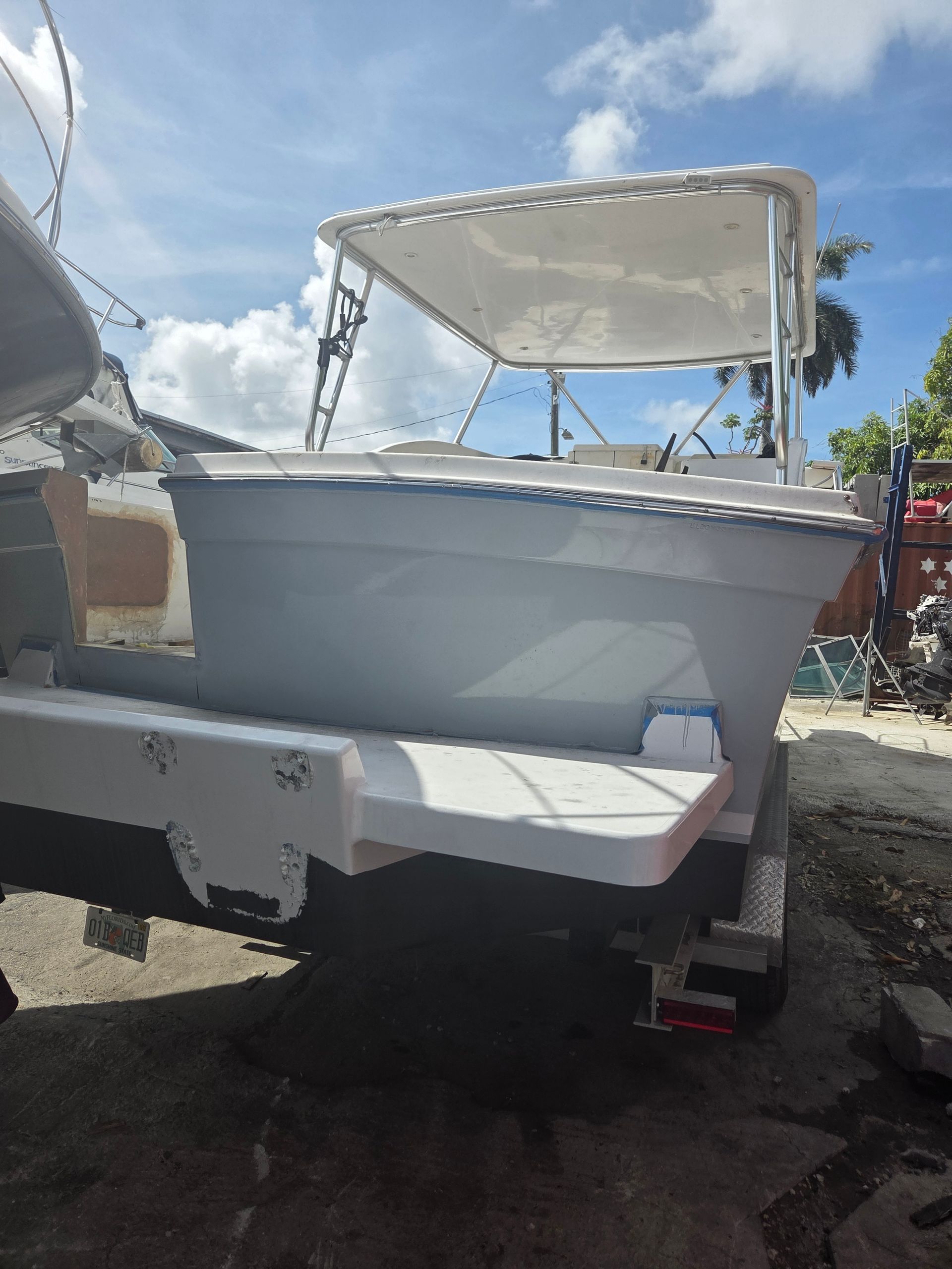 Gray boat on a trailer, white sunshade, blue sky, sunny day.
