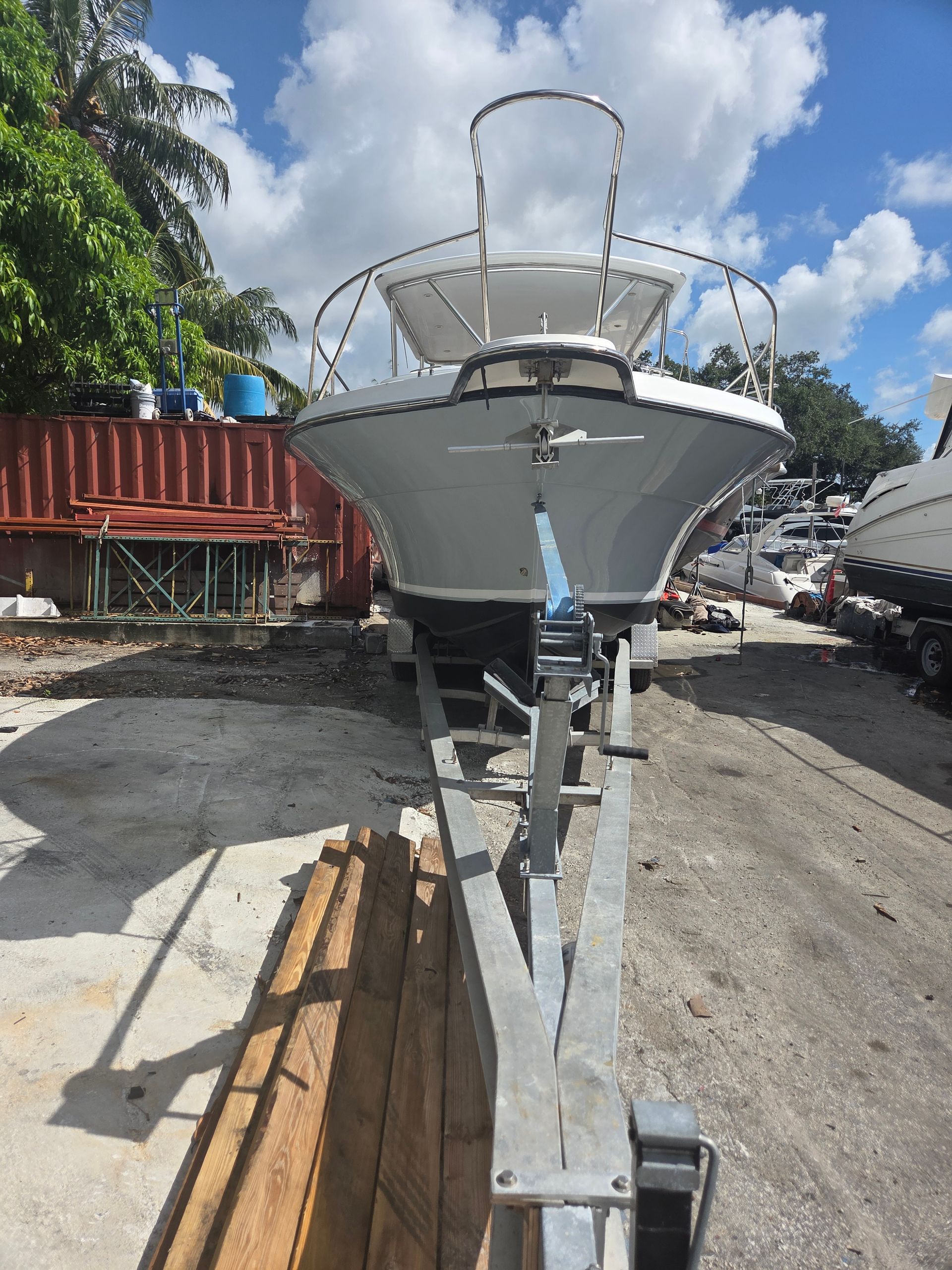 White boat on a trailer, viewed head-on, outdoors. Trailer on a concrete surface with debris.