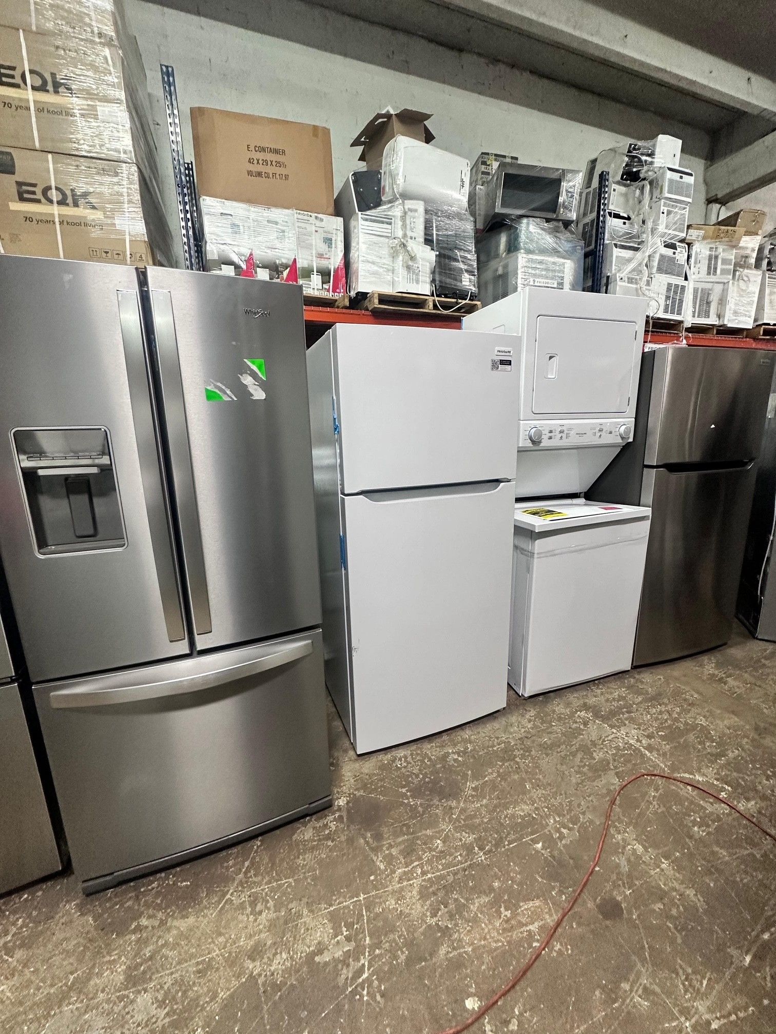 Refrigerators and appliances in a warehouse.  A stainless steel fridge is on the left.