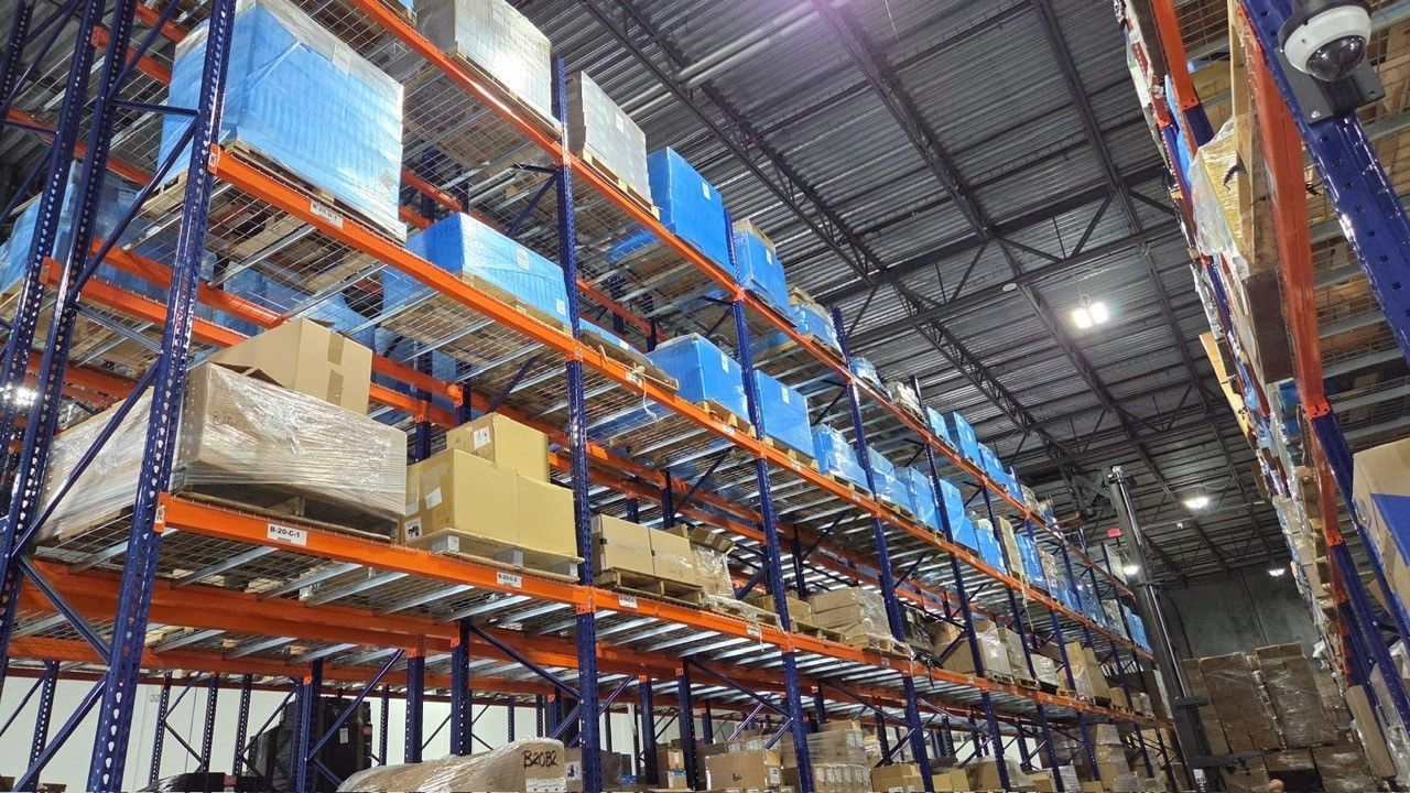 Warehouse interior with tall orange and blue shelving filled with boxes and wrapped pallets.