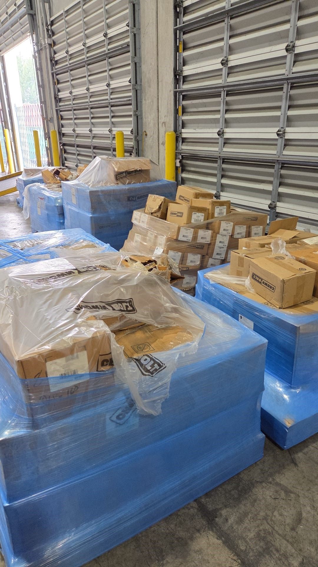 Pallets wrapped in blue plastic hold boxes in a warehouse loading dock.