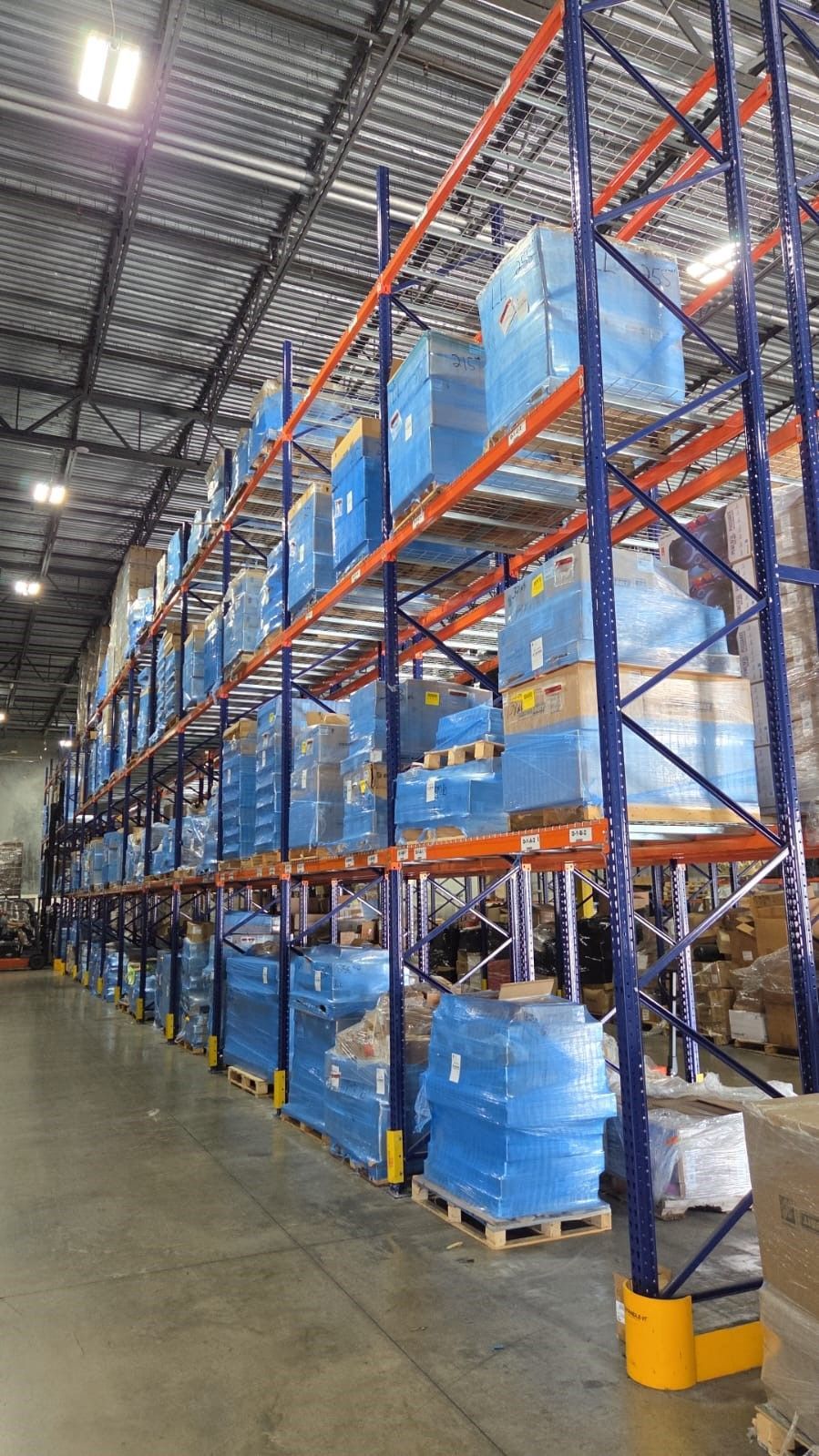 Warehouse with tall blue and orange shelving filled with wrapped pallets.