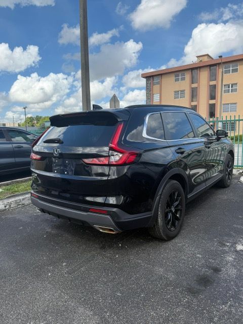 Black Honda CR-V SUV parked outdoors on a sunny day. Building and fence in the background.