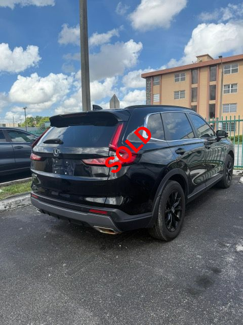 Black Honda CR-V SUV parked outdoors on a sunny day. Building and fence in the background.