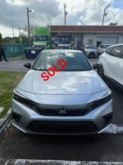 Silver Honda Civic parked in front of a building with trucks in the background.