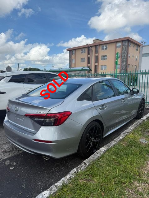 Silver Honda Civic parked next to a curb in front of a building with blue sky.