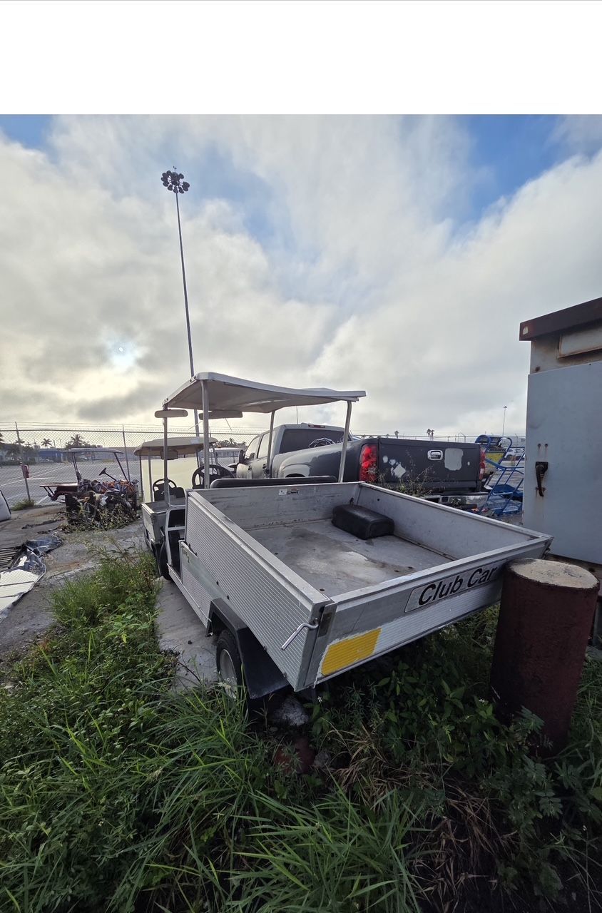 White utility cart with a canopy parked near a grassy area, with a cloudy sky background.