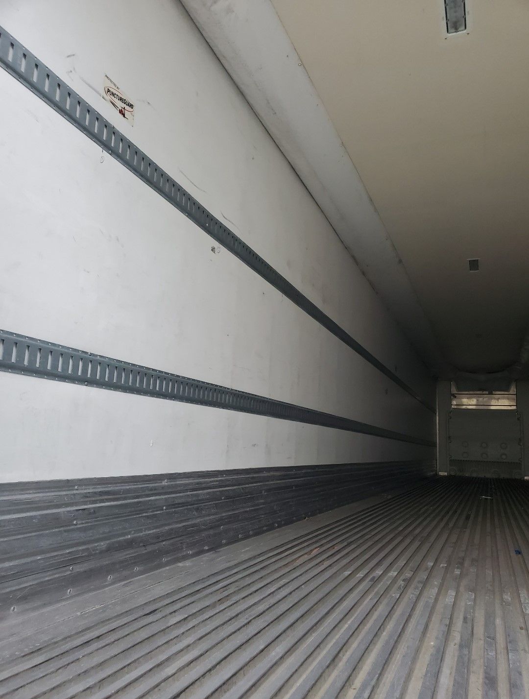 Interior view of a refrigerated truck trailer with white walls, black floor, and metal tracks.
