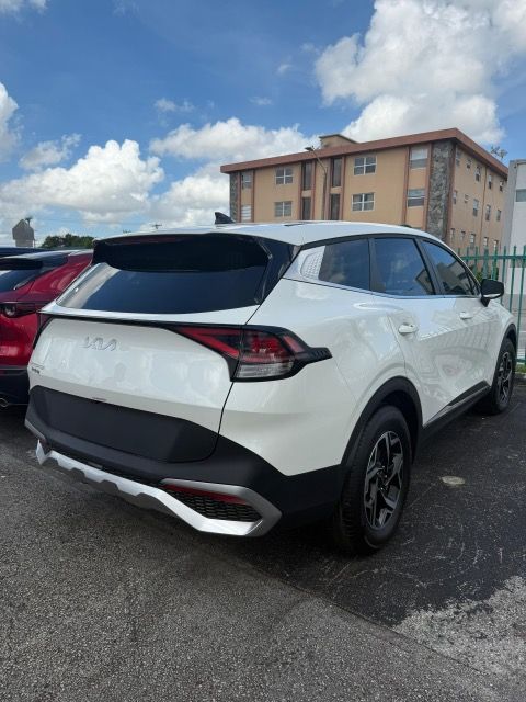 White Kia Sportage SUV, parked outdoors, under a blue sky, black accents on bumper.