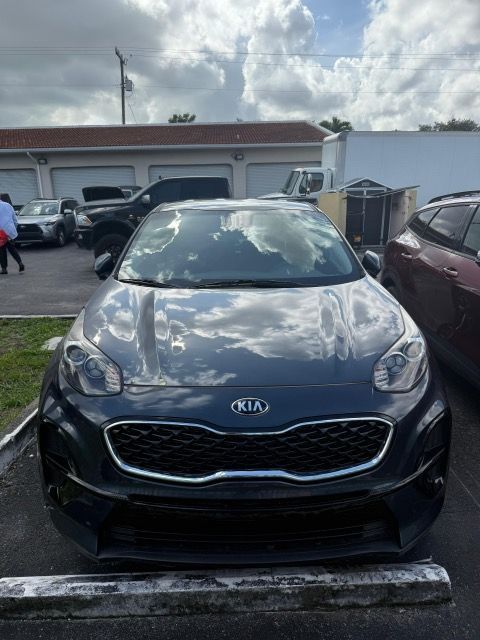 Dark gray Kia Sportage SUV parked outdoors, with a cloudy sky reflected in the windshield.
