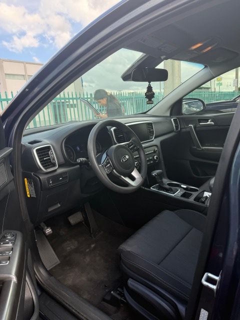 Interior of a dark blue Kia Sportage. A person outside the car cleans the windshield.