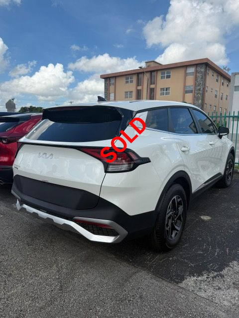 White Kia Sportage SUV, parked outdoors, under a blue sky, black accents on bumper.