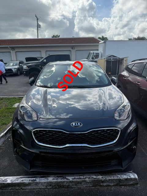 Dark gray Kia Sportage SUV parked outdoors, with a cloudy sky reflected in the windshield.