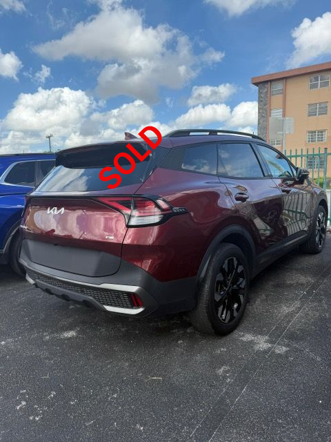 Red Kia Sportage SUV parked outdoors under a cloudy sky.