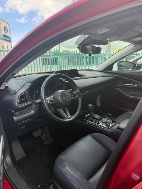 Interior of a red Mazda, black dashboard, steering wheel, seats, and console. Bright sky visible.