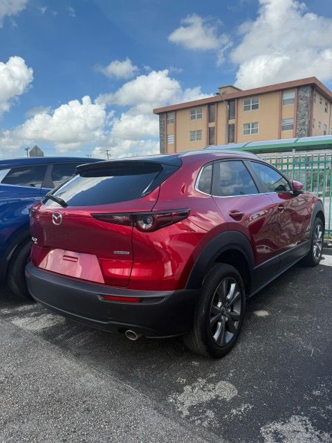 Red Mazda CX-30 SUV parked outdoors with a blue sky background and a building.